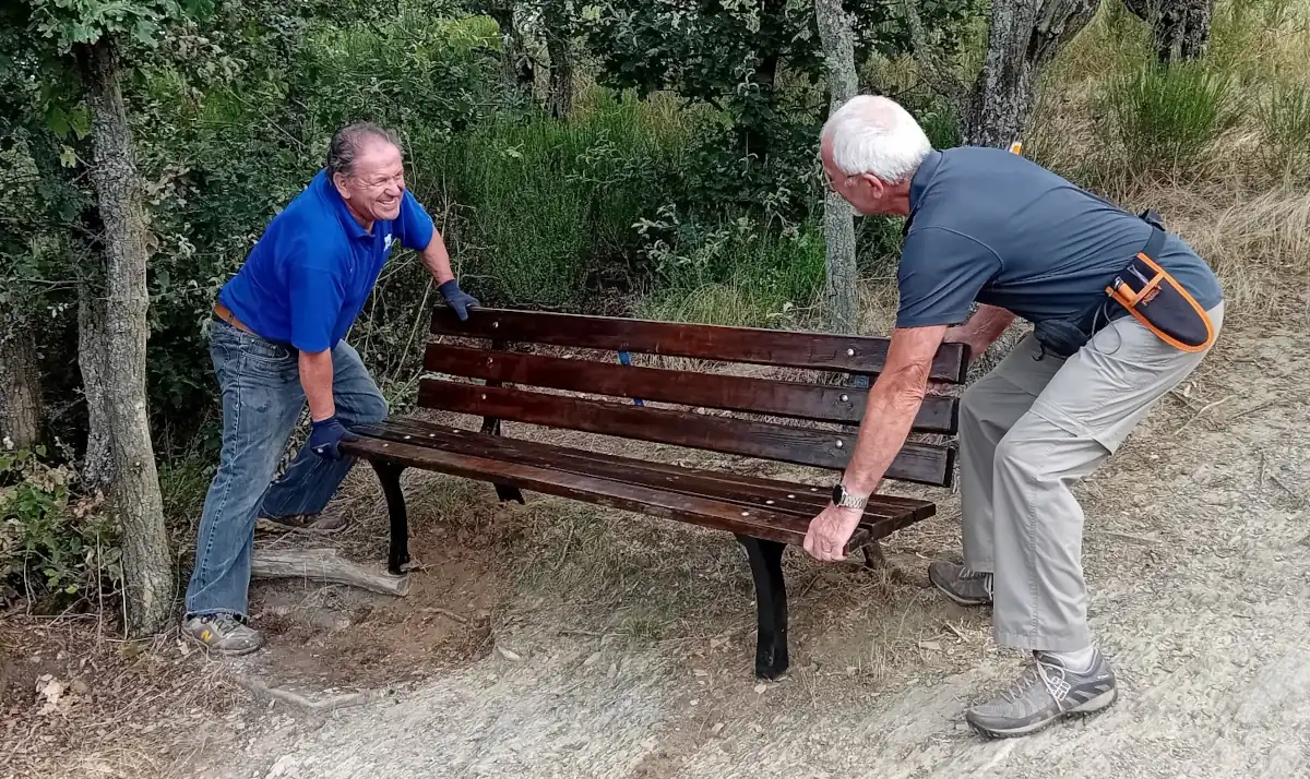 2 Männer stellen eine Bank am Wanderweg auf. 