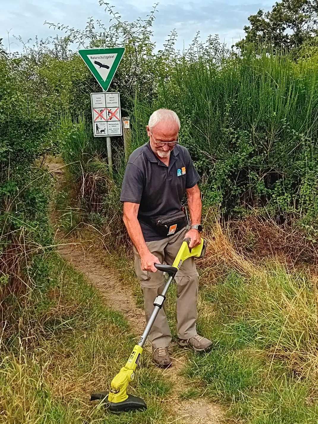 Hermann Nördershäuser entfernt mit einem Freischneider Unkraut auf dem Wanderweg. 